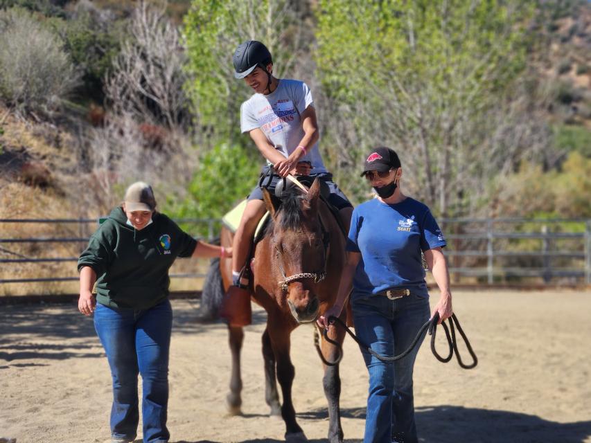 Camper riding a horse along with two Painted Turtle side walkers 
