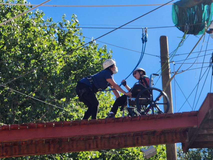 A camper being assisted on the ropes course by a counselor