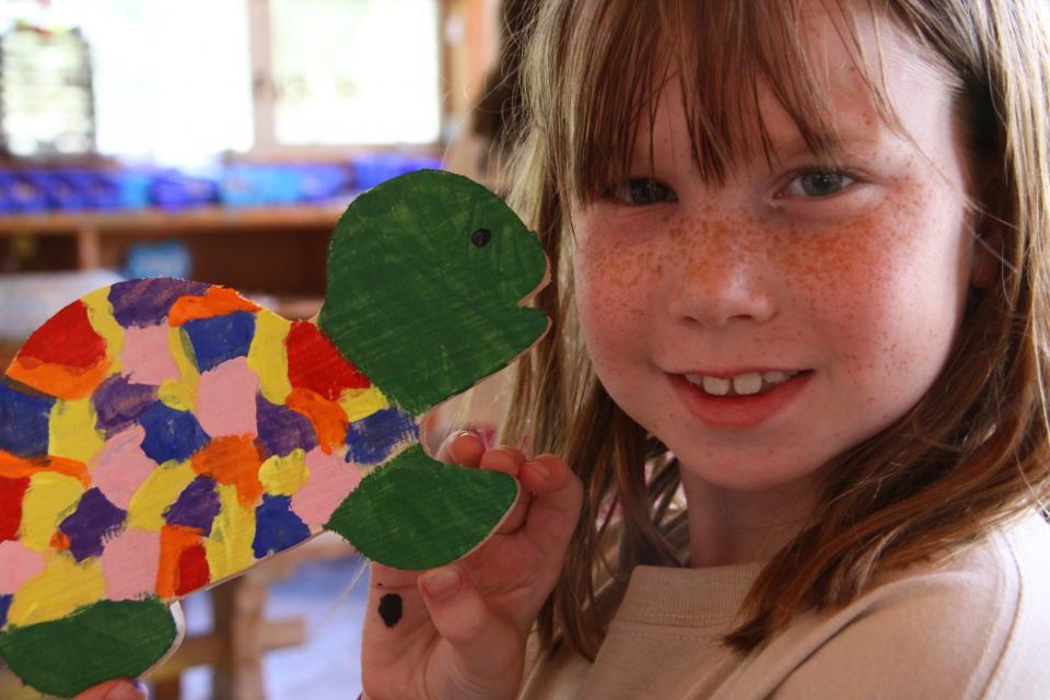 Girl holding a wooden turtle she painted in Arts and Crafts
