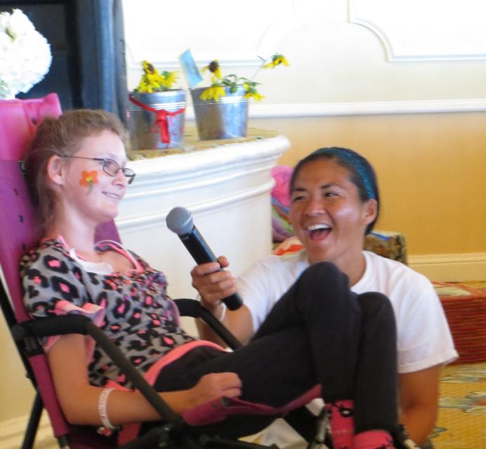 April Tani, Director of Programs and Initiatives kneeling down to holds a microphone up for a camper using a wheel chair to speak into
