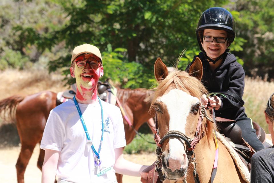Equestrian volunteer with boy enjoying horseback riding.